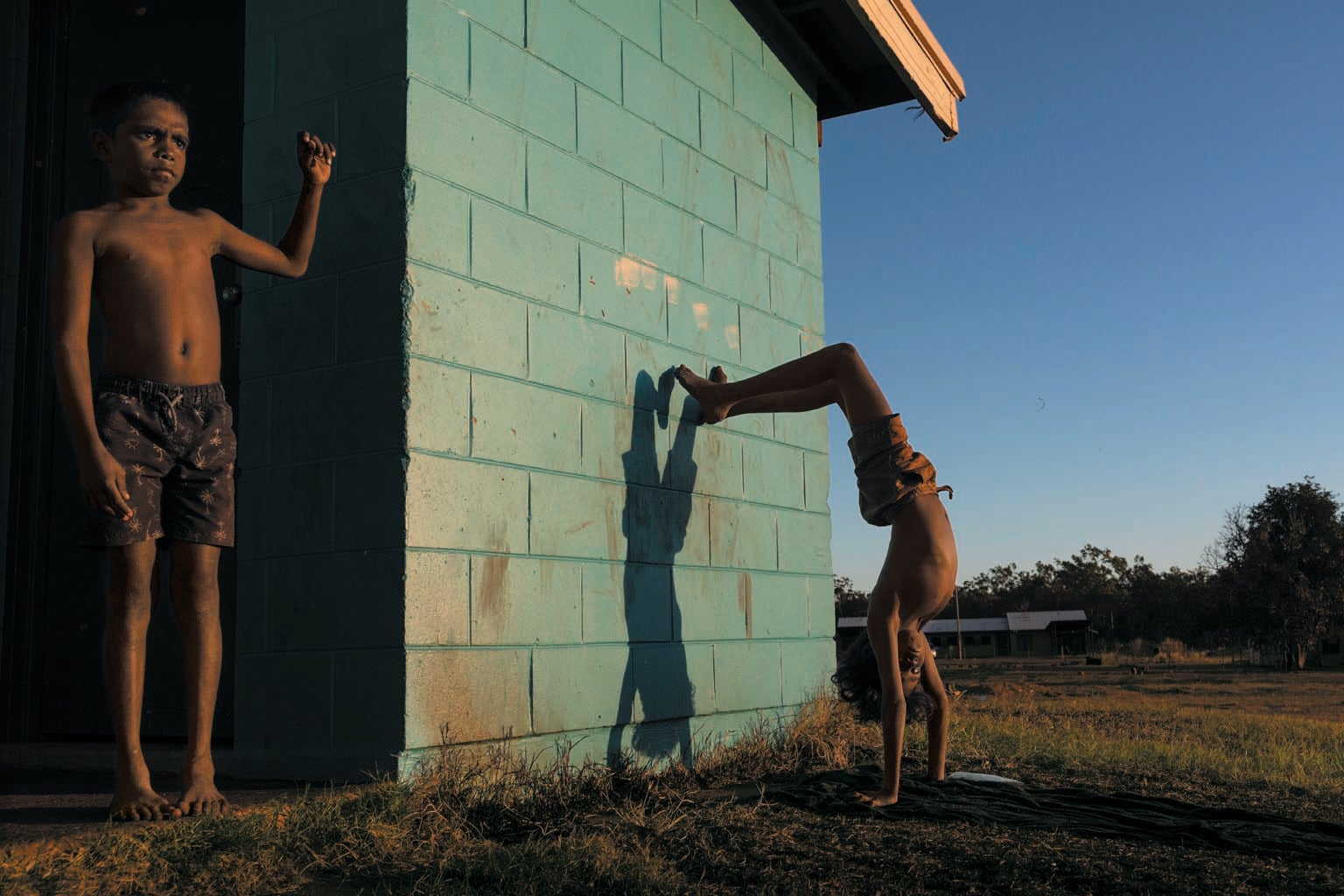 Two children playing outside a building. One child is doing a handstand against the building.