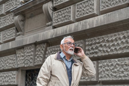 An Older Man is Talking in the City Streets and Having a Serious Conversation Using his Smart Phone.