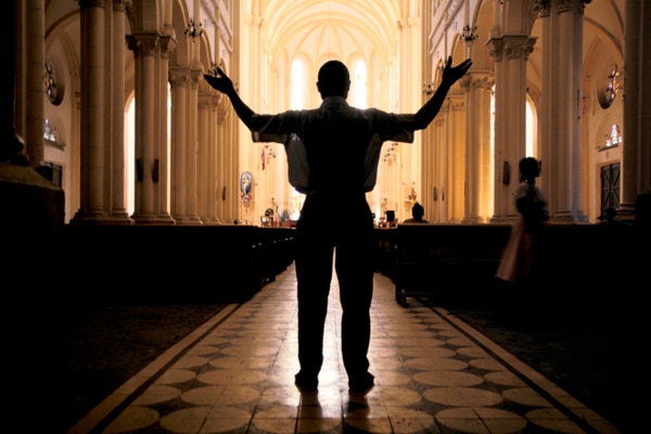 A man raises his arms in prayer inside a catholic cathedral.