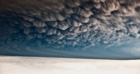 Dramatic landscape, with snow on ground and dark gray ash clouds filling the sky and forming consistent pattern.