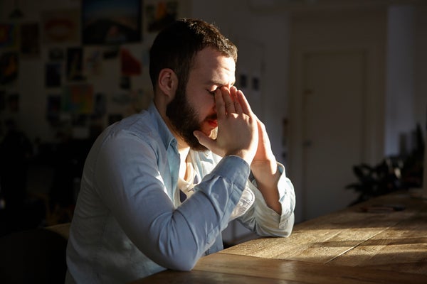 Young man sitting at kitchen table with hands on face.