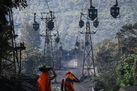 Workers in orange wrap walk beneath a line of cable trolleys