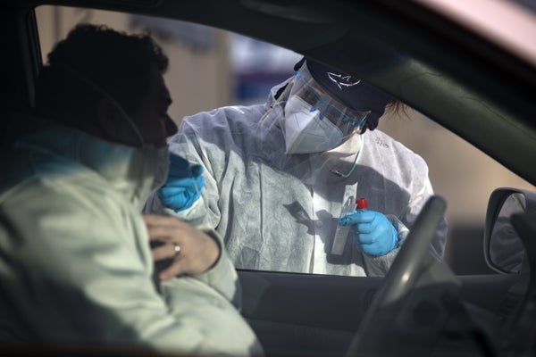 A healthcare worker performs a COVID test on a man in a car.