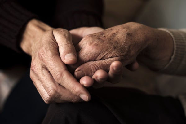 A closeup showing both hands of a younger person holding one hand of an older person.