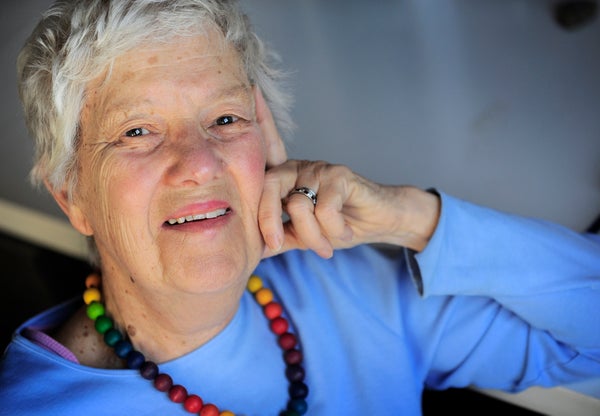 An older woman in a blue top wearing a necklace, smiling broadly.