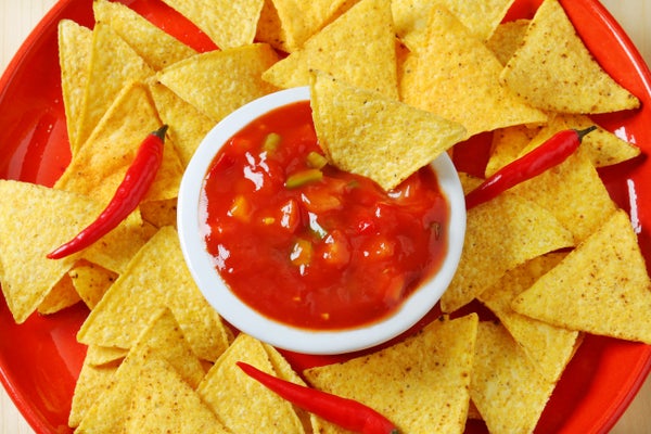 Tortilla chips on a red plate with salsa dip and chili peppers