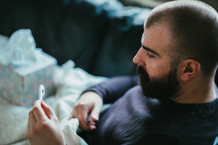 Sick man lying down in bed and measuring temperature