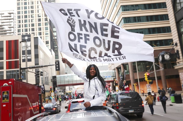 A woman holds a banner that reads "Get Your Knee Off Our Necks."