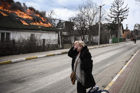 Woman covers face as she passes house on fire.