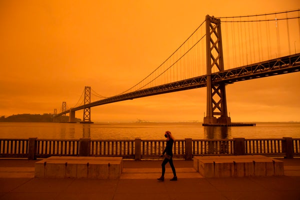 Woman walking against eerie orange sky polluted by wildfire.