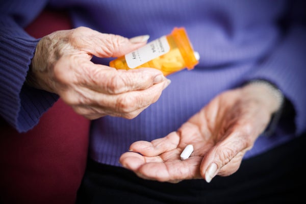 Mid section of a senior woman's hands in purple sweater holding a prescription bottle dispensing a pill.-