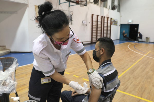 A healthcare worker gives a vaccine to a seated man.  AHMAD GHARABLI/AFP via Getty Images)