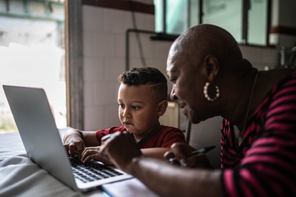 Grandmother helping grandson to study on laptop at home