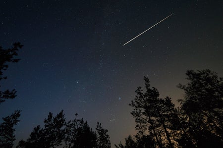 Night scene with starry sky and meteorite trail over forest. Long exposure shoot