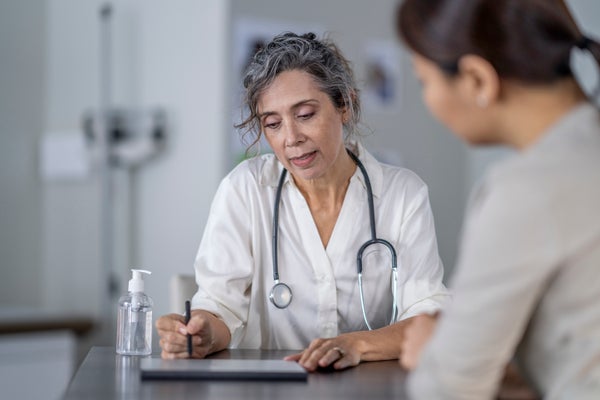 A mature female doctor points to the screen of her tablet laying out on the table in front of her as she shares her patients test results with her