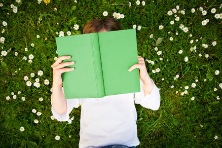 Child laying on grass reading book.