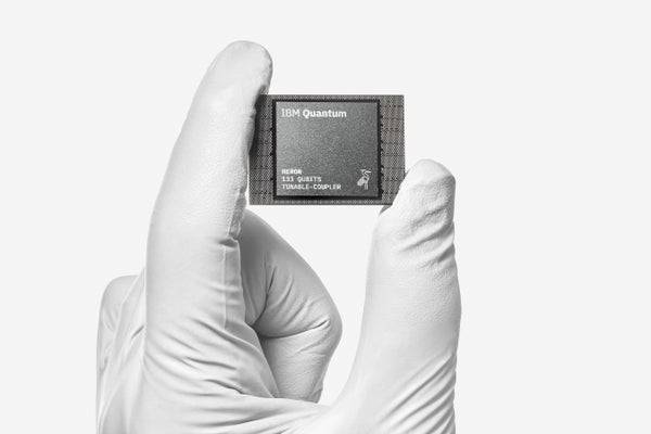 One of IBM's latest quantum processor chips held up by a hand in white rubber gloves.
