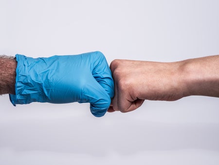 Two hands, one in a medical glove, do a fist bump.