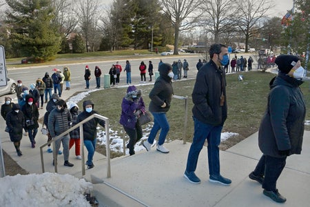 Masked people lined up on the steps of a library