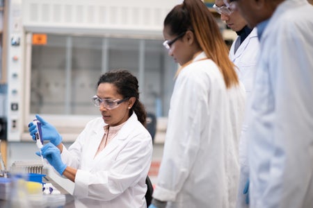 Four scientists of different sexes and ethnic backgrounds gather around a lab bench.