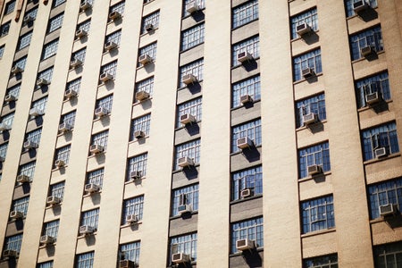 Individual air conditionars poke through the windows of a tall building.