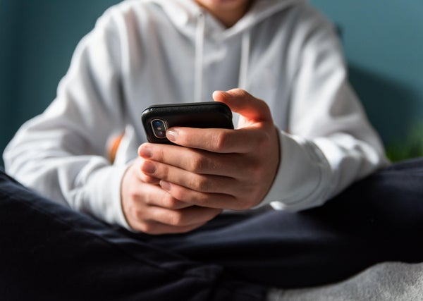 Close up of hands of teen boy in white sweater scrolling on phone.