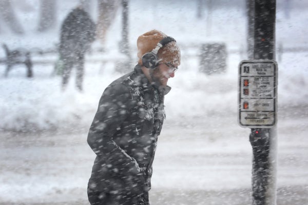 A pedestrian with headphones walks through a snow storm.