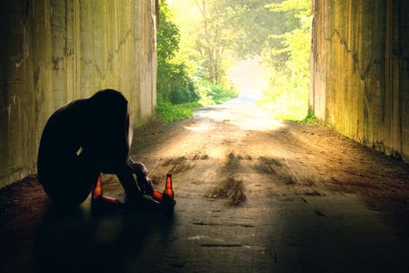 A person in a tunnel in silhouette with empty beer bottles.