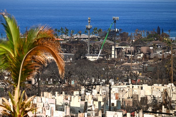 Utility workers are seen in the distance repairing cell phone service towers surrounded by structures destroyed by fire