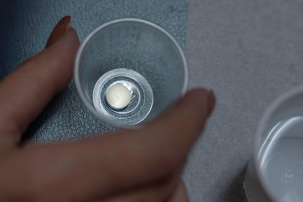 A hand holds a small plastic cup containing a single pill