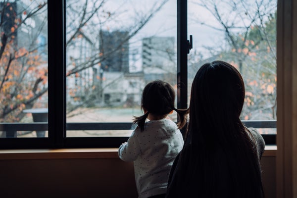 Rear view of young Asian mother and little daughter looking through window