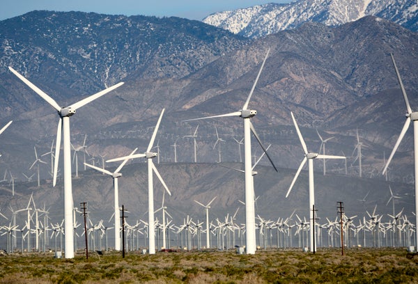 Dozens of wind turbines operating before a snow-capped mountain