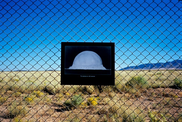 A sign showing the explosion of an atomic bomb is hanging on a chainlink fence in front of the Trinity Test Site