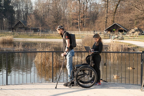 Gert-Jan walks with the assistance of a crutch, scientist following him w/ wheel chair.