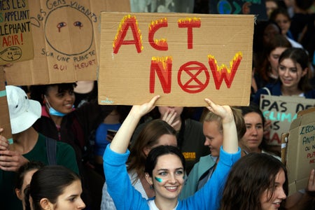 Woman in blue shirt holding an ACT NOW sign written with w/ red flames