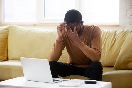 A seated man lifts his glasses to rub his eyes.