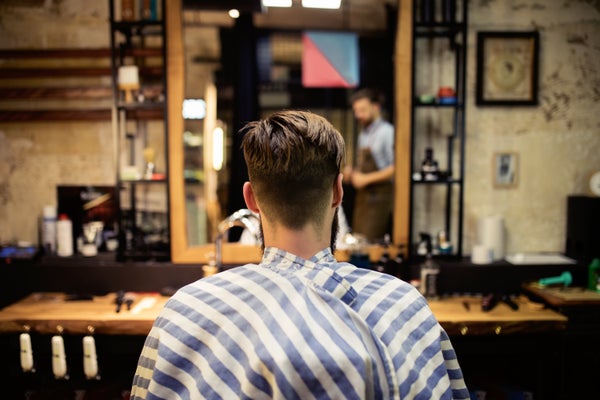 A barber's first-person view of the back of their client's head sitting in a chair in front of a mirror