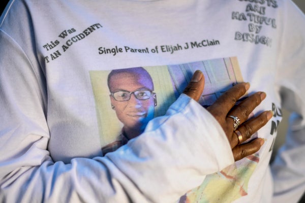 Close-up of Sheneen McClain's touching her sweater with her son Elijah's photo with text: "Single Parent of Elijah J. McClain."