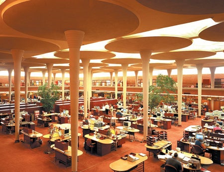 Wide and elevated view of an open office plan space with very high ceilings and interior architectural support columns.