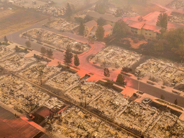 Aerial view of a burned down neighborhood covered in bright orange fire retardant.